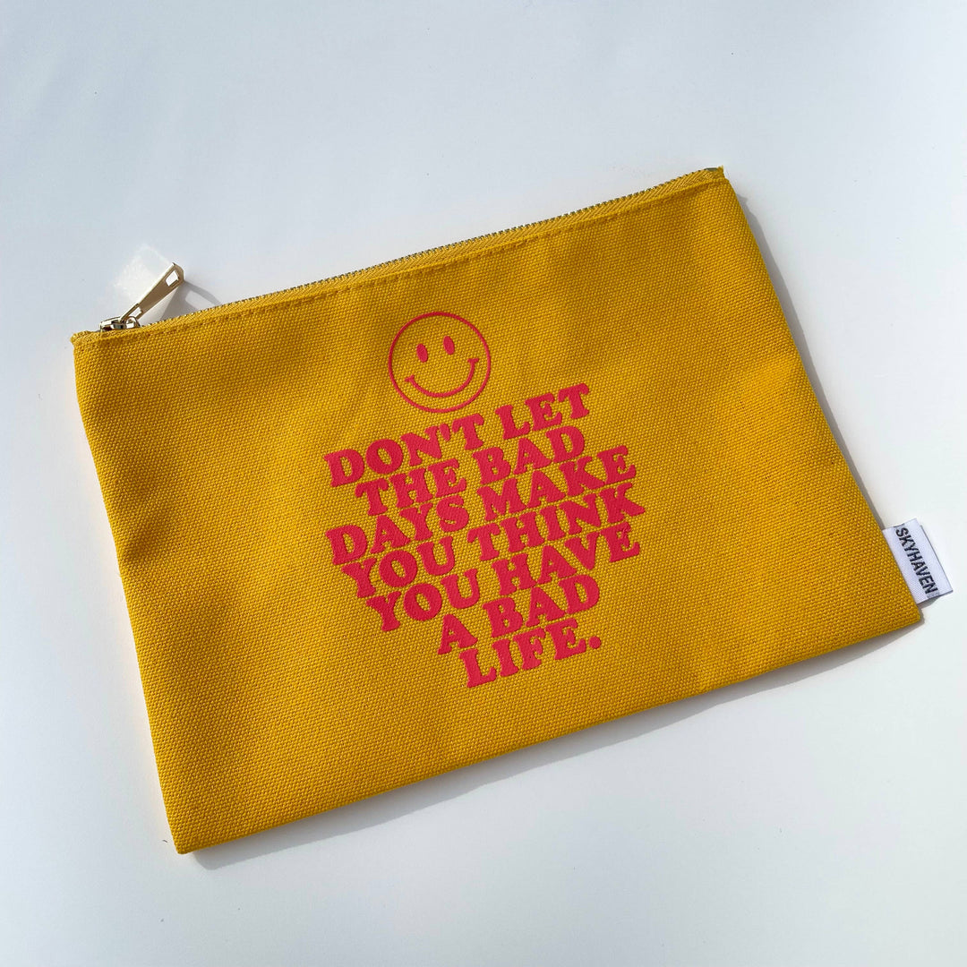 mustard yellow canvas pouch with the words "Don't let the bad days make you think you have a bad life" printed in dark pink with a smiley face at the top